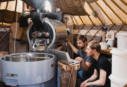 Two men sitting and looking at a laptop at a coffee roasting food manufacturing facility.