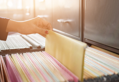 A filing cabinet that is opened and a hand is pulling a document out of the drawer.