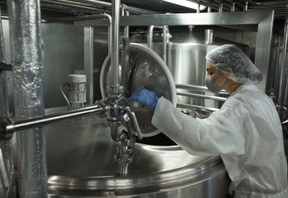 A person wearing protective equipment and checking a tank in a food factory.