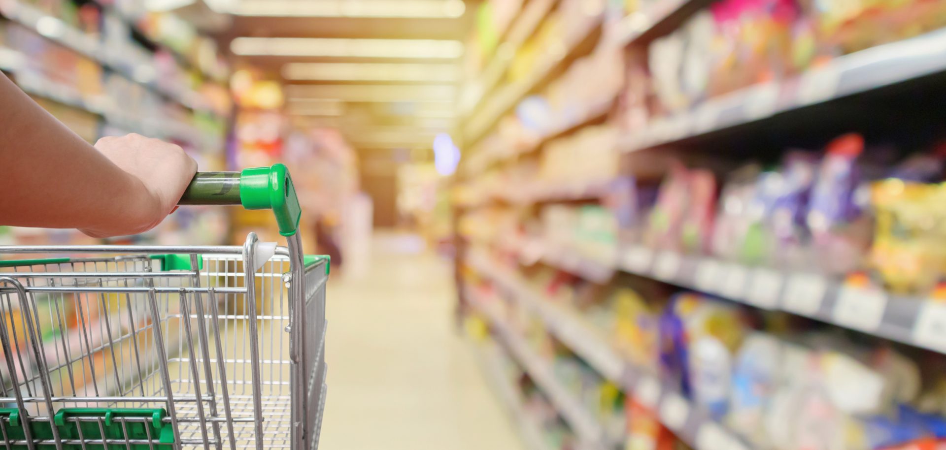 Grocery cart with an aisle in a grocery store with products that are likely certified by the process of a third party audit.