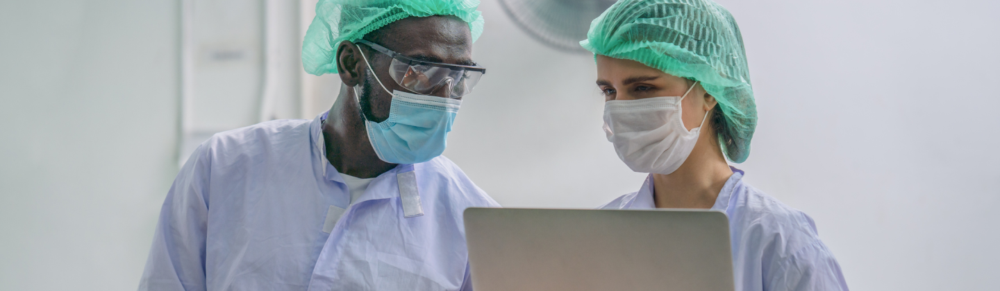 a man and a woman wearing masks and looking at a computer while performing Quality management system consulting.