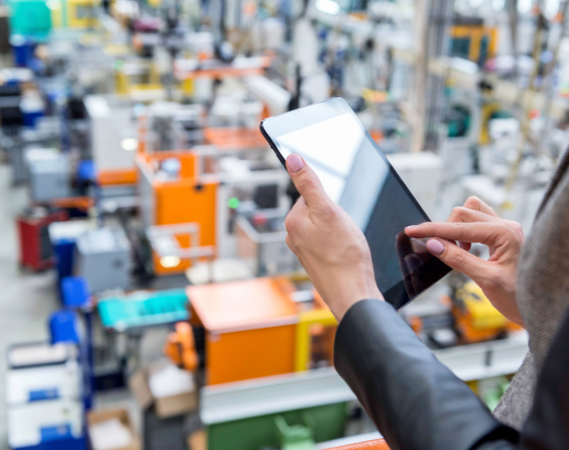 Manufacturing environment in the background with a woman's hands holding an electronic device and touching the screen.