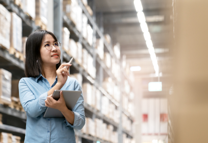 A woman walking around a manufacturing facility performing an internal audit pointing to storage shelves.