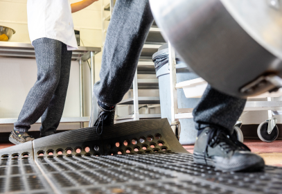 Risk assessment to prevent trips and falls in food facilities. Person's foot is tripping over mat.