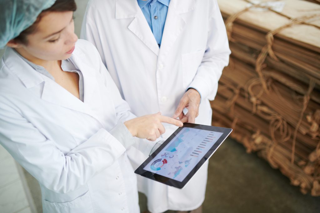 Two people wearing white lab coats and looking at an electronic screen while they appear to be discussing food safety & quality topics.